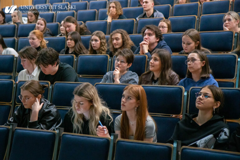 Grupa młodzieży siedząca w auli. Jedni uważnie słuchają, inni robią notatki.